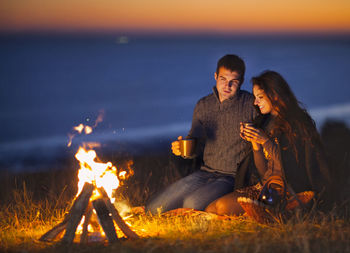 Man and woman sitting on bonfire by land against sky