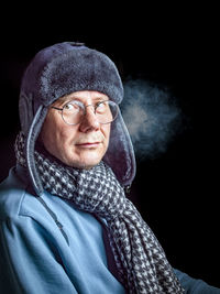 55-year-old man in trapper hat and warm winter clothes isolated on a dark background. frosty vapor.
