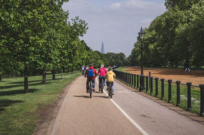 Rear view of people riding bicycle on road against sky