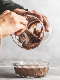 Close-up of hand holding bowl of chocolate mousse batter pouring into glass bowl