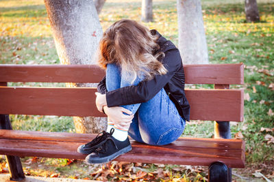 Sad teenager girl sitting on the bench in autumn park. crying young girl in puberty