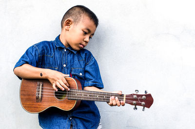 Boy playing guitar against wall