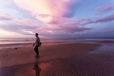 Full length of man standing on beach against sky during sunset
