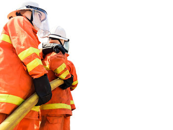 Low angle view of firefighters holding fire hose against clear sky