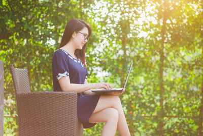 Side view of woman using laptop while sitting on chair