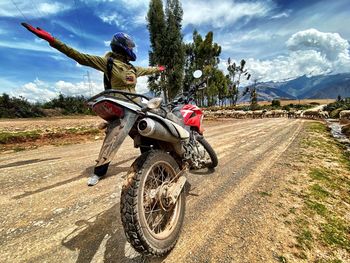 Woman standing by motorcycle on road against cloudy sky