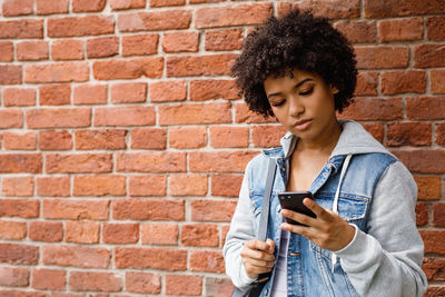 Young woman looking away while standing against brick wall