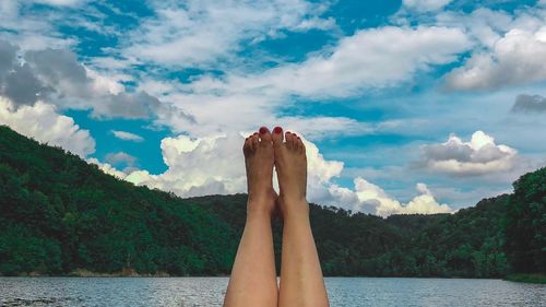 Low section of woman relaxing on water against sky