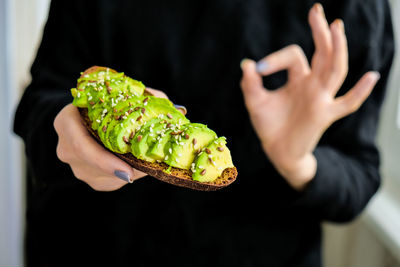 Female hand holding healthy avocado toast. ripe hass avocado, wholegrain bread, sesame flax seeds. 