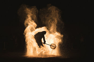Silhouette man performing stunt in fire at night