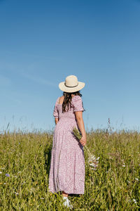 Rear view of woman standing on meadow, holding bouquet of wildflowers