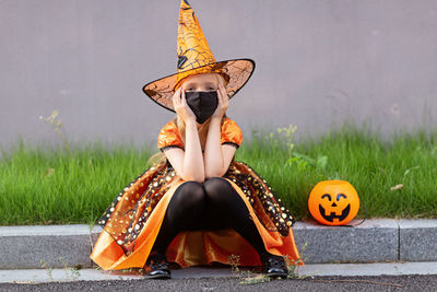 Full length of woman sitting against stone wall during halloween