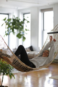Smiling woman with arms raised relaxing on hammock at home