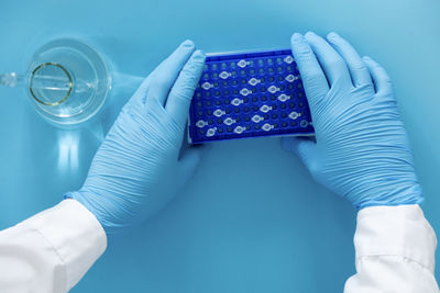 Midsection of doctor holding dentures against blue background
