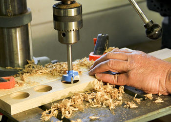 Cropped hand of carpenter drilling wood on table