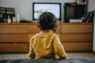 Rear view of girl watching tv at home