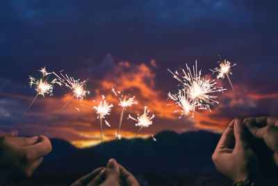 Cropped hand holding sparkler at sunset