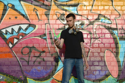 Full length of young man standing against graffiti wall