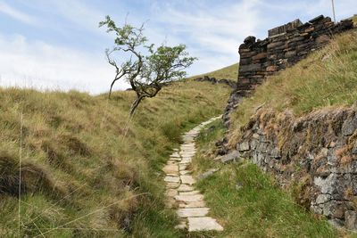 View of packhorse trail leading up hillside by stone wall with sky