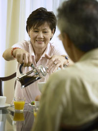 Close-up of smiling woman serving coffee to senior man on table