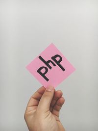 Cropped hand holding paper with php text on it against white background