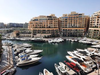 Sailboats moored on river by buildings in city against sky