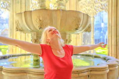 Woman with arms outstretched standing against fountain