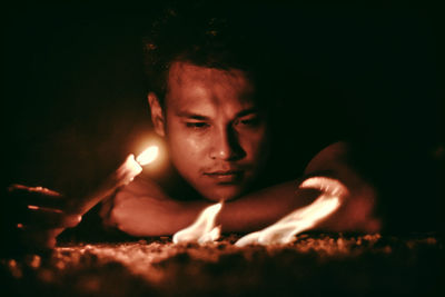 Close-up of young man by lit candle at night