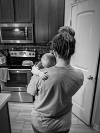 Rear view of woman with baby standing in kitchen