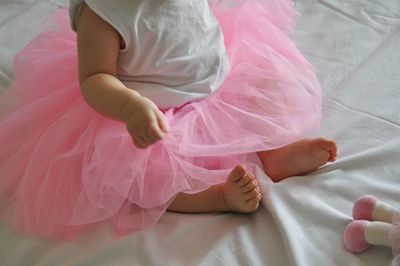 Low section of baby girl in pink dress sitting on bed