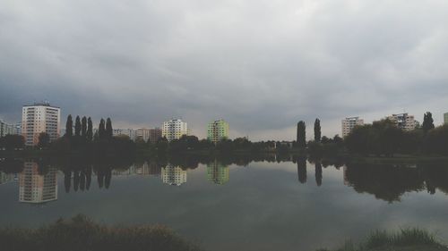 Reflection of buildings in calm lake against cloudy sky