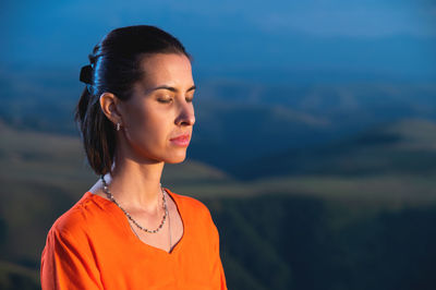 Beautiful dreamy woman meditating outdoors with closed eyes, with blur effect on dark green nature