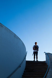 Low angle view of man standing on staircase against clear blue sky