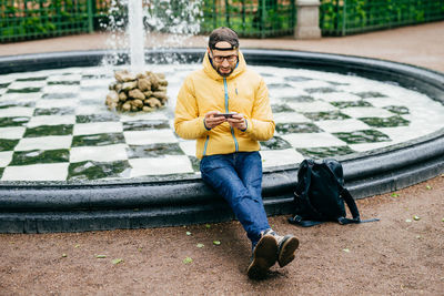 Full length of young man sitting by water