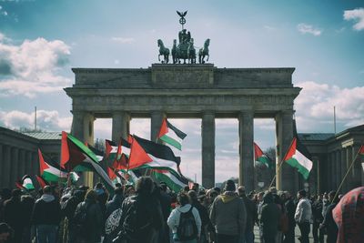 Crowd waving palestinian flags at brandenburg gate against sky