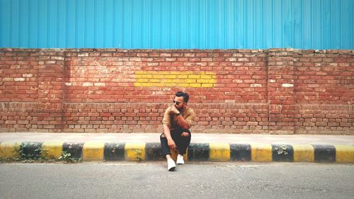 Full length of shirtless man standing against brick wall