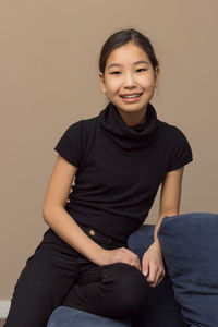Portrait of a smiling young woman sitting against wall