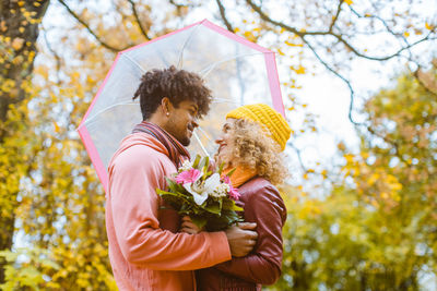 Couple standing with umbrella against trees during autumn