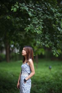 Side view of young woman standing by trees on field