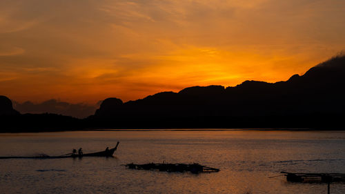 Silhouette boats in sea against orange sky