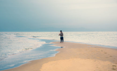 Man playing flute while standing at beach against sky