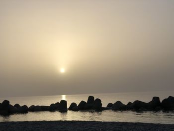 Silhouette rocks on sea against sky during sunset