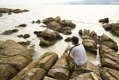 Rear view of woman sitting on rock at beach