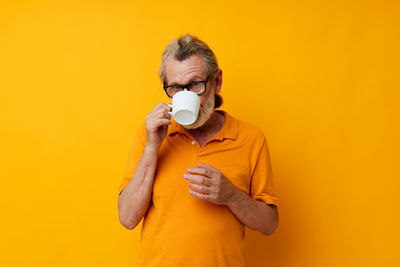 Portrait of senior man drinking coffee against yellow background