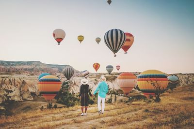 Rear view of couple looking at hot air balloons flying over land against sky