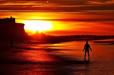 Silhouette man on beach against orange sky during sunset