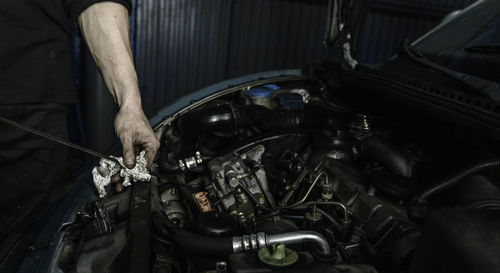 Crop unrecognizable repairman using car's dipstick to measure engine oil level