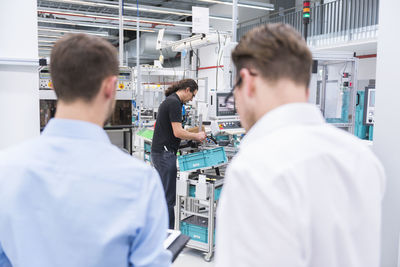 Two businessmen in factory shop floor with man in background working