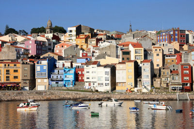 Boats in river by townscape against clear blue sky