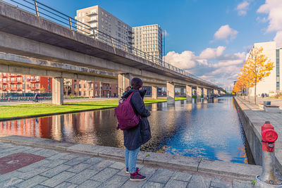 Woman stands near canal near a bridge of a subway line in the Ørestad district copenhagen, denmark